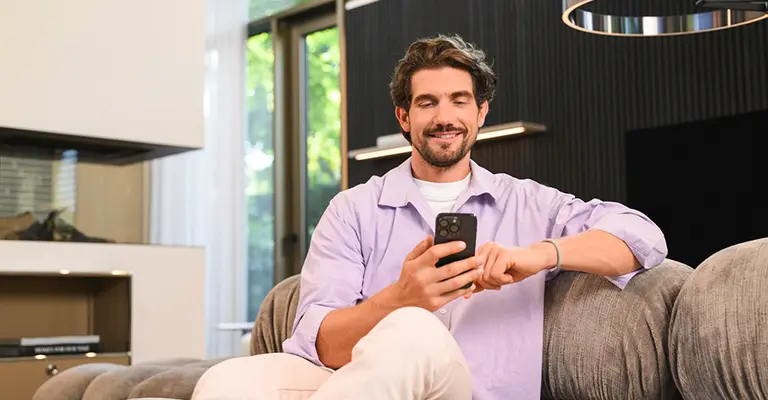 Ein Mann sitzt auf dem Sofa mit dem Smartphone und registriert BW-Secure für seine Mercedes Creditcard