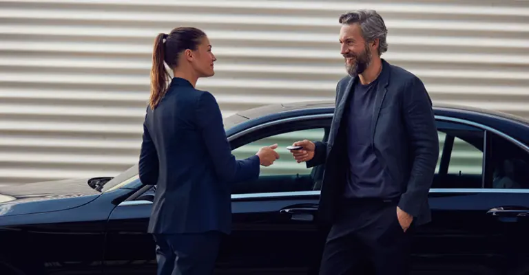 Ein Mann holt bei einer Frau seinen Mietwagen mit der Mercedes Credit Card ab
